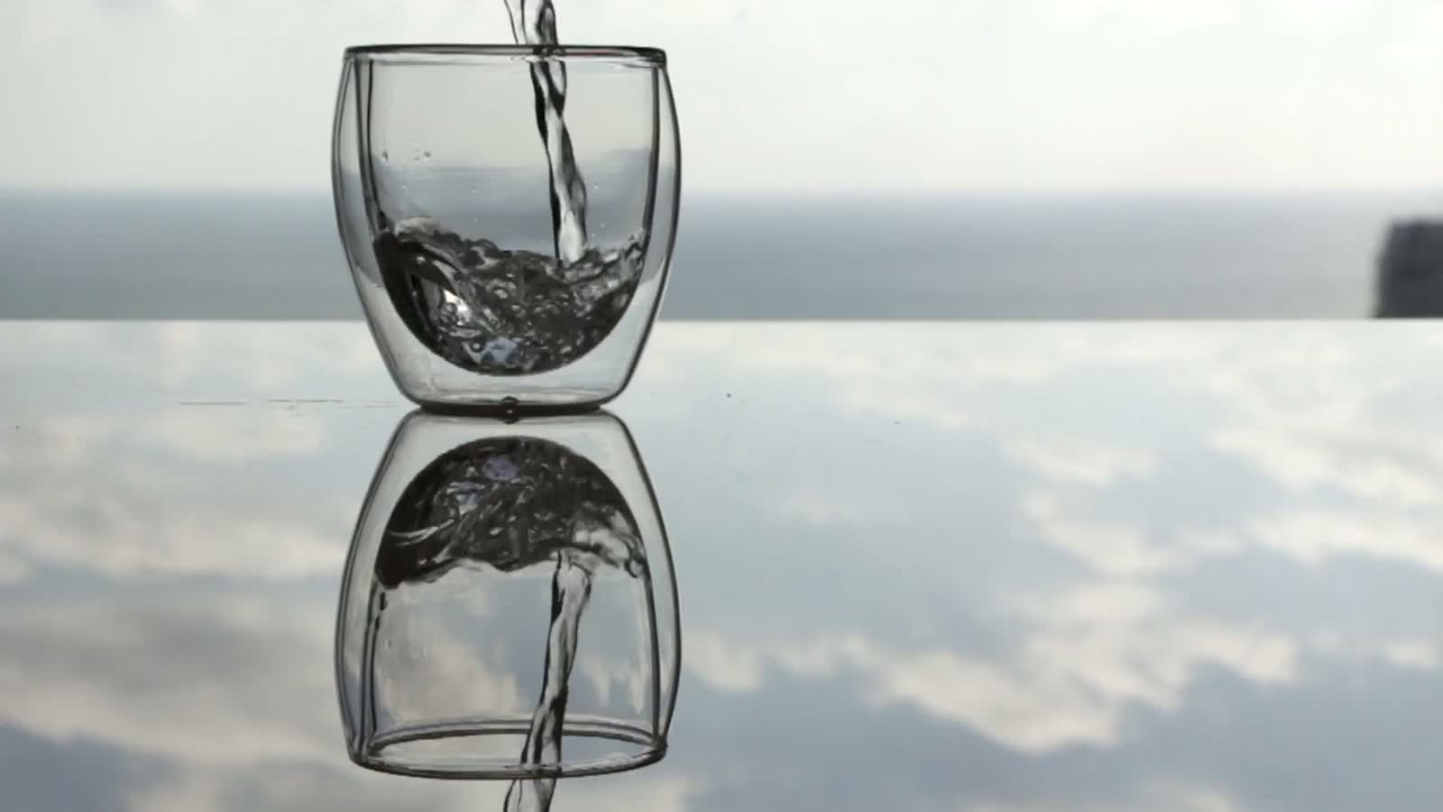 A clear glass being filled with water in bright daylight