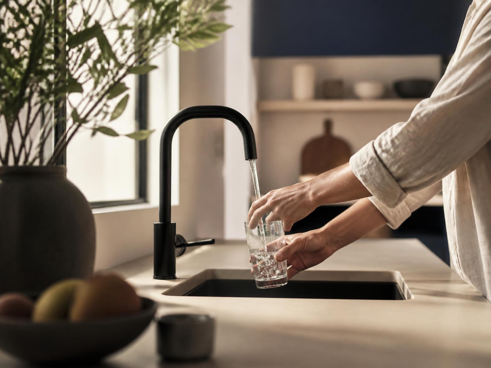 A parent filling a clear glass of water at a kitchen faucet in morning light