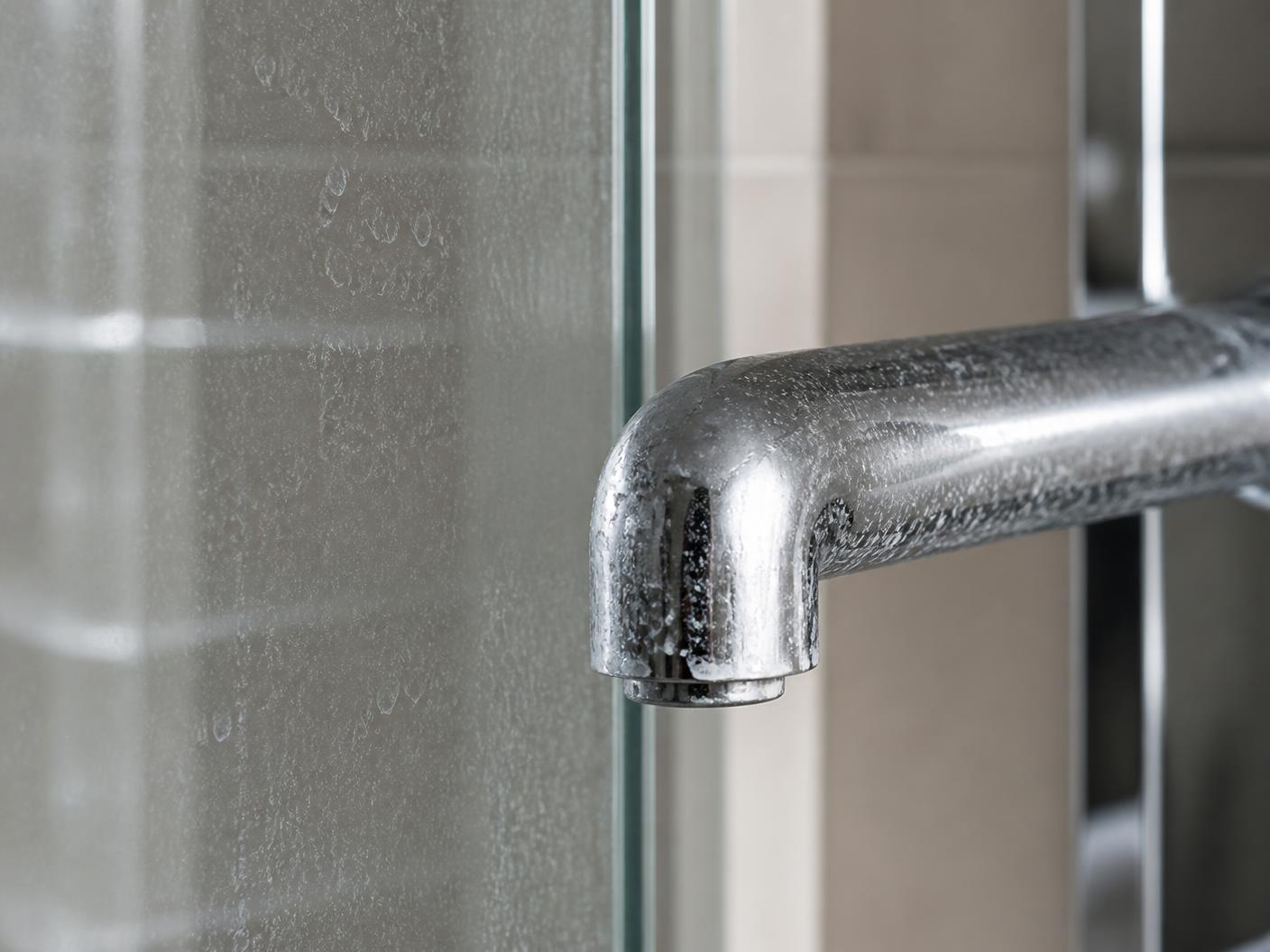 Close-up of mineral spotting on a glass shower enclosure and a chrome faucet
